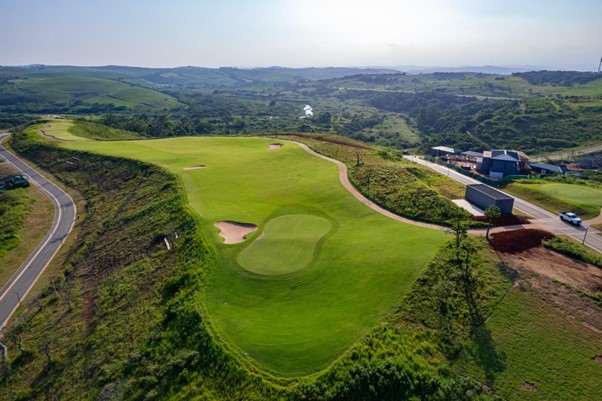 Aerial view of a green golf course surrounded by rolling hills and homes.