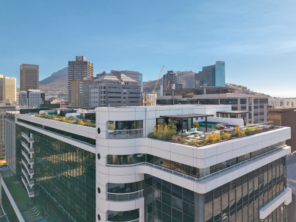 The Onyx seen from across the Foreshore, a curved white tower with green roof gardens and penthouse terraces along its top floor, Cape Town CBD and Signal Hill behind