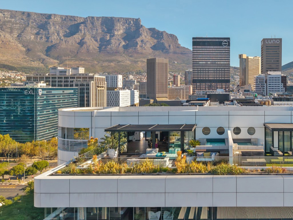 The top of The Onyx photographed from an adjacent building, showing the penthouse roof terrace with pergola, seating and two heated pools, Table Mountain in the background