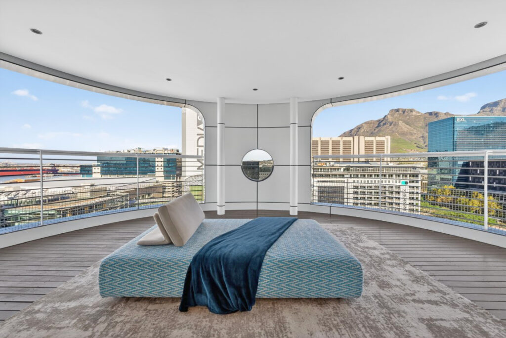 A curved open terrace on the penthouse roof level with a daybed between arched openings, looking towards Devils Peak and the harbour