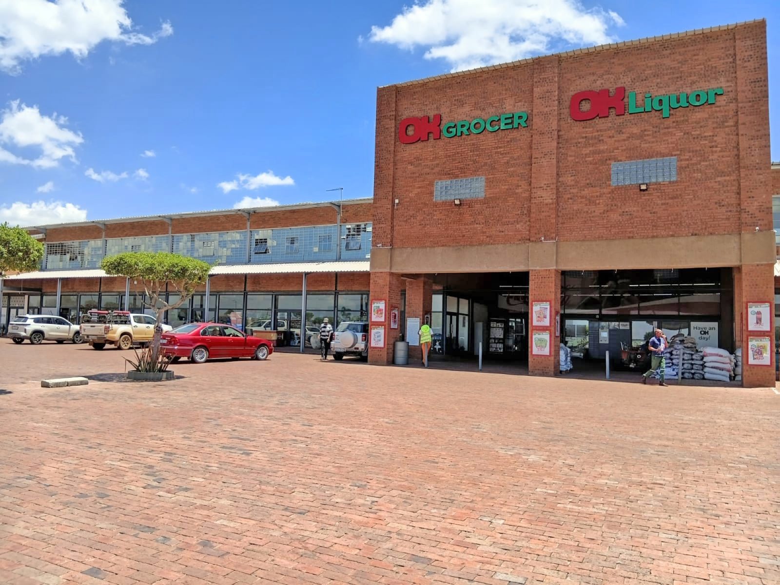 The brick frontage of the OK Grocer and OK Liquor stores at Wadrif, seen across a paved parking area under a blue sky.