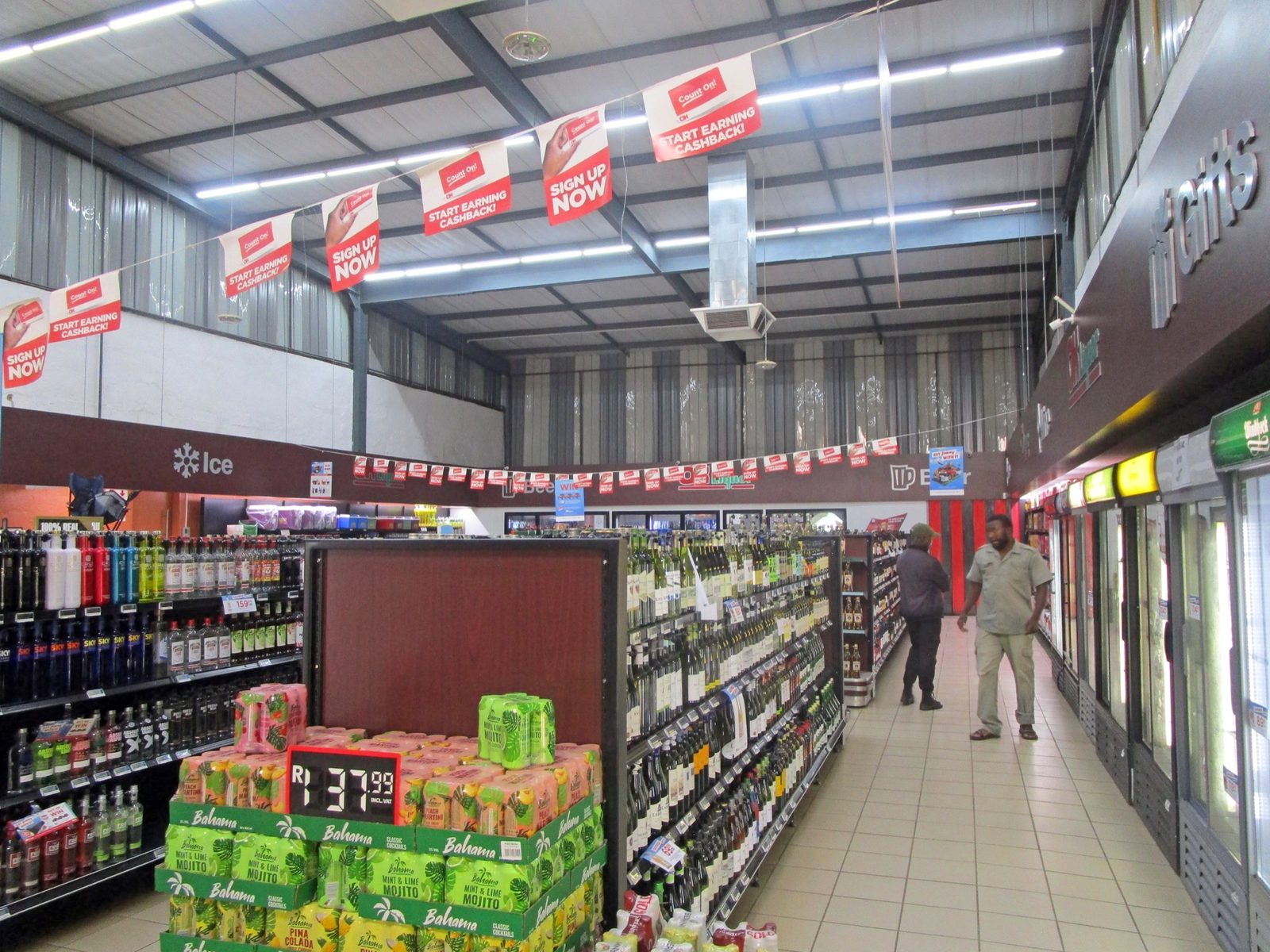 Aisles inside the OK Liquor store, stacked with crates and bottles under a high warehouse roof.