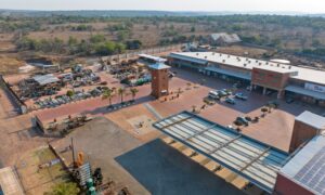 Aerial view of the Wadrif node showing long warehouse roofs, a loading yard with trucks and the retail frontage facing the R573.