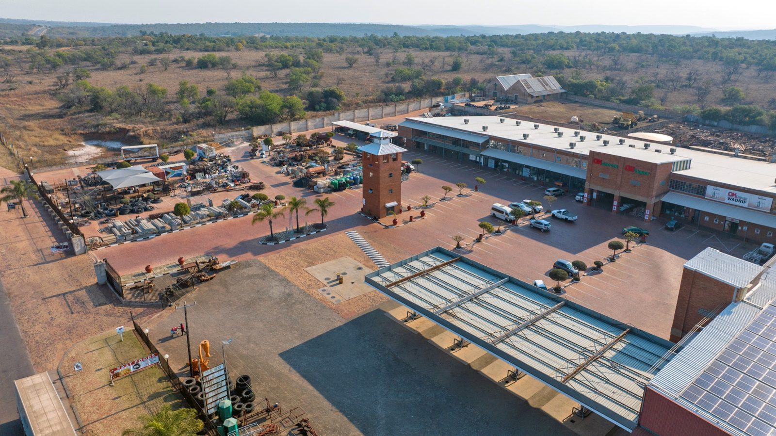 Aerial view of the Wadrif node showing long warehouse roofs, a loading yard with trucks and the retail frontage facing the R573.